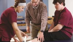 A student practices bandaging another students leg with the help of an instructor