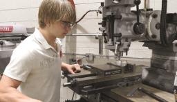A student with safety glasses uses a piece of machinery 