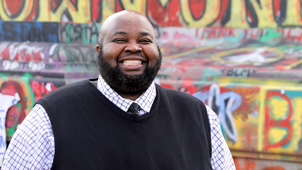 teacher of the year rodney robinson smiles brightly in front of a graffitied statue 