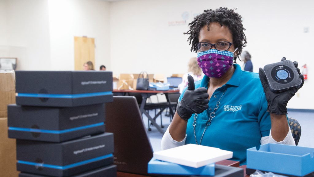 as school staff member in a mask holds up electronic equipment and gives a thumbs up to the camera