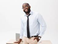 a black male teacher stands near his desk and smiles at the camera