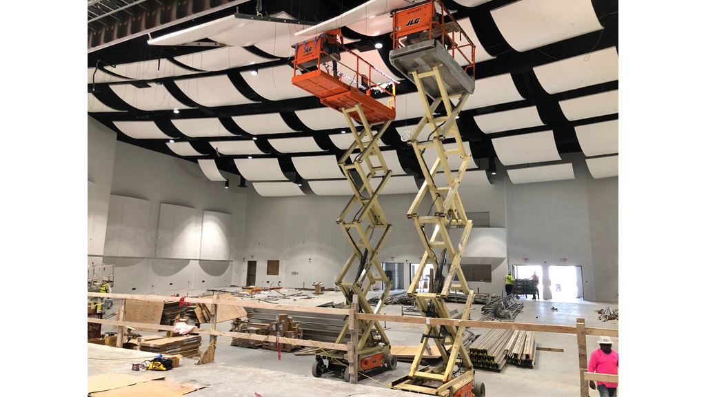 a florida school auditorium under construction, with scissor lift vehicles reaching high up to the ceiling