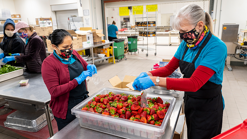 Two food service employees put fresh strawberries in bags