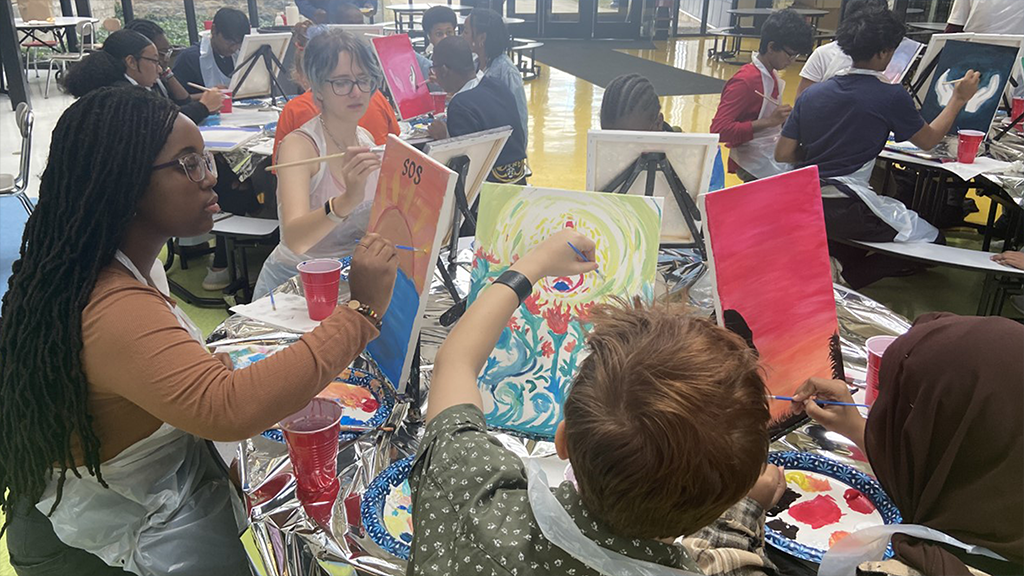 A group of high school students paint on canvases during an art class. 