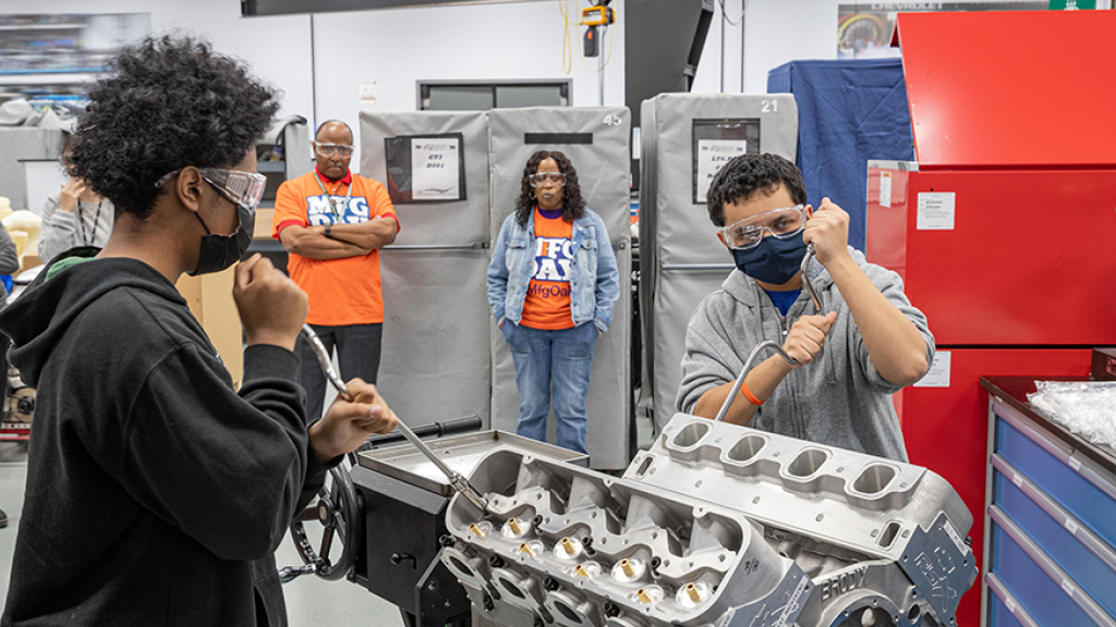 An instructor helps a student examine a car engine 