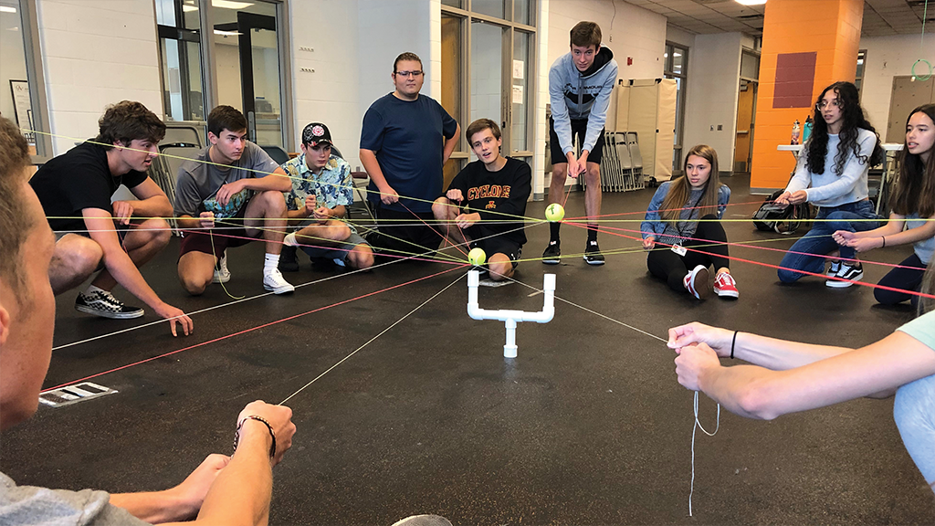 A group of high school students sit on the floor participating in a team-building exercise. 
