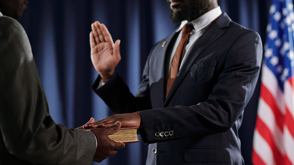 A man places one hand on top of a bible as he raises the other hand to take the oath of office.