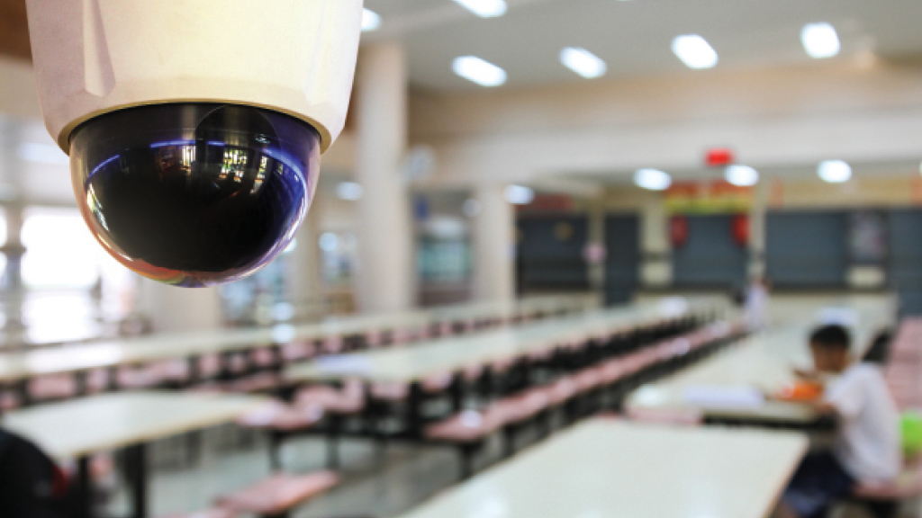In a school cafeteria, a dome-shaped security camera is positioned in the ceiling.