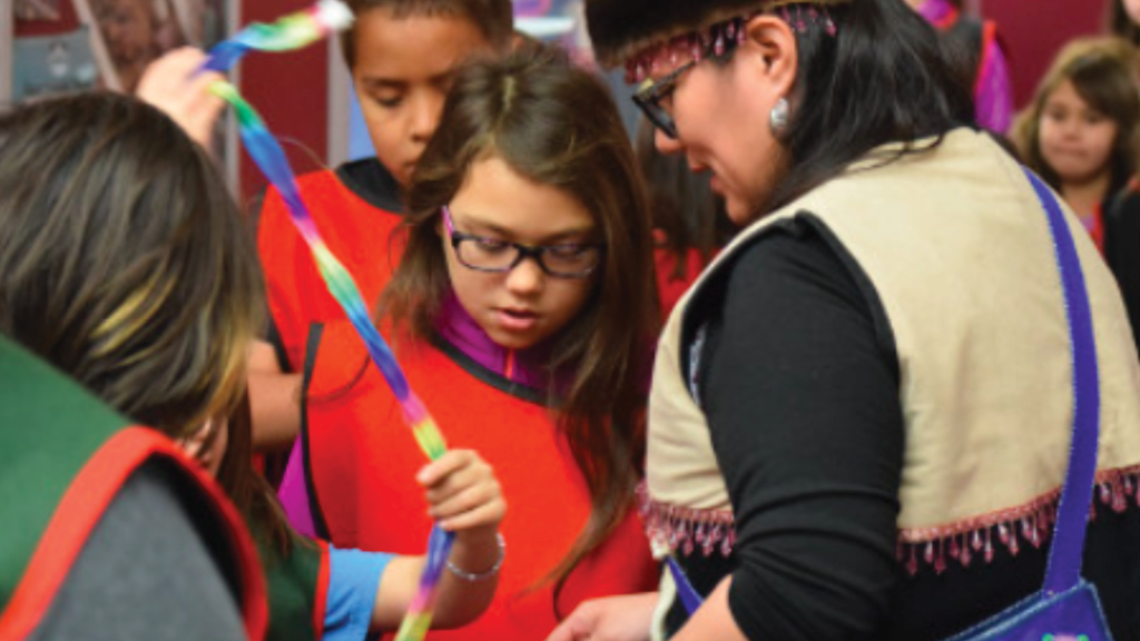 A group of Alaska native students examine traditional clothing and ornaments.  