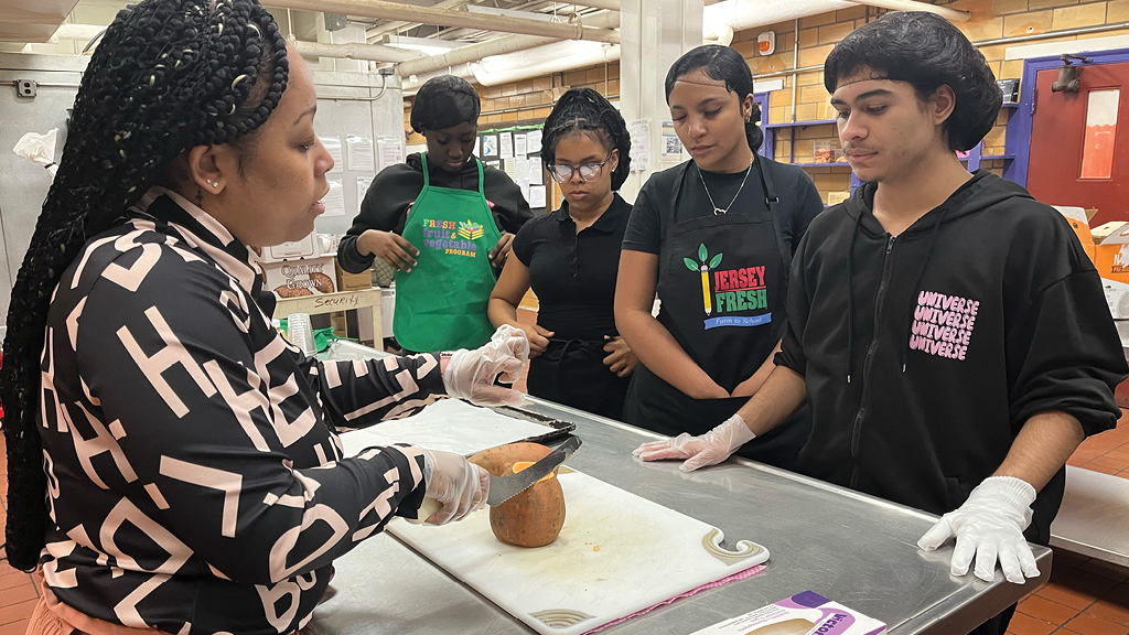 A school chef demonstrates cutting a sweet potato as students watch