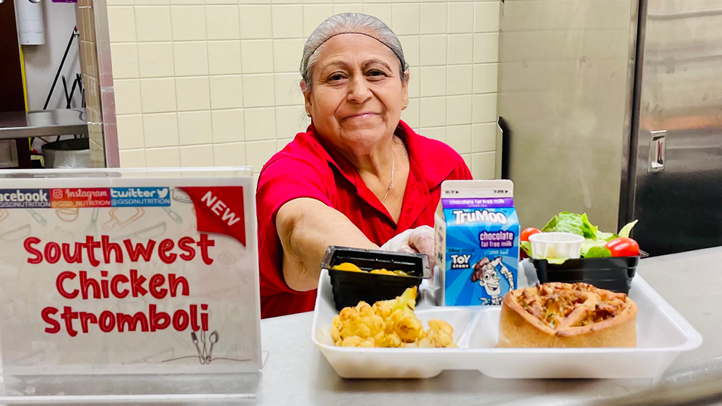 A school cafeteria worker offers a tray of food.