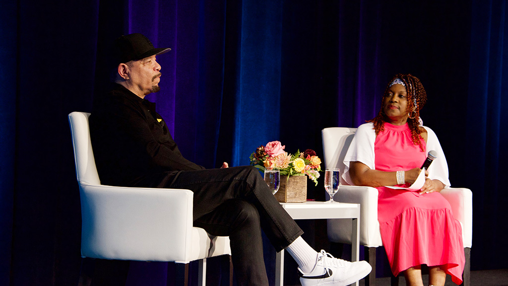 The actor and singer Ice T sits in a chair on stage for a conversation with a woman also seated in a chair. 