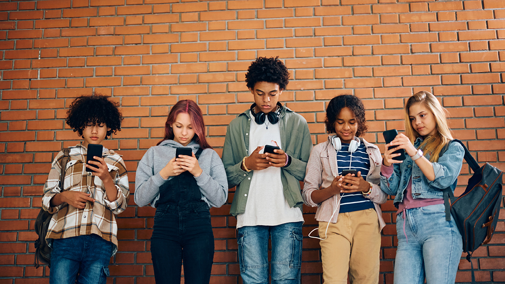 a group of six male and female high school students stare into their cellphones