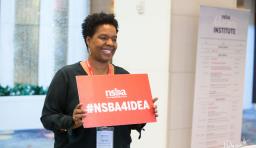 a conference attendee holds up a sign that says "NSBA4IDEA"