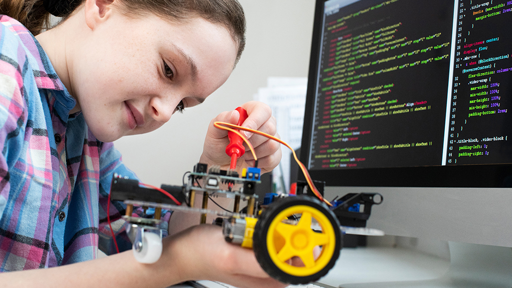 a student builds a robot, she is sitting in front of a computer displaying lines of code