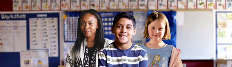 Three kids in a classroom look at the camera and smile